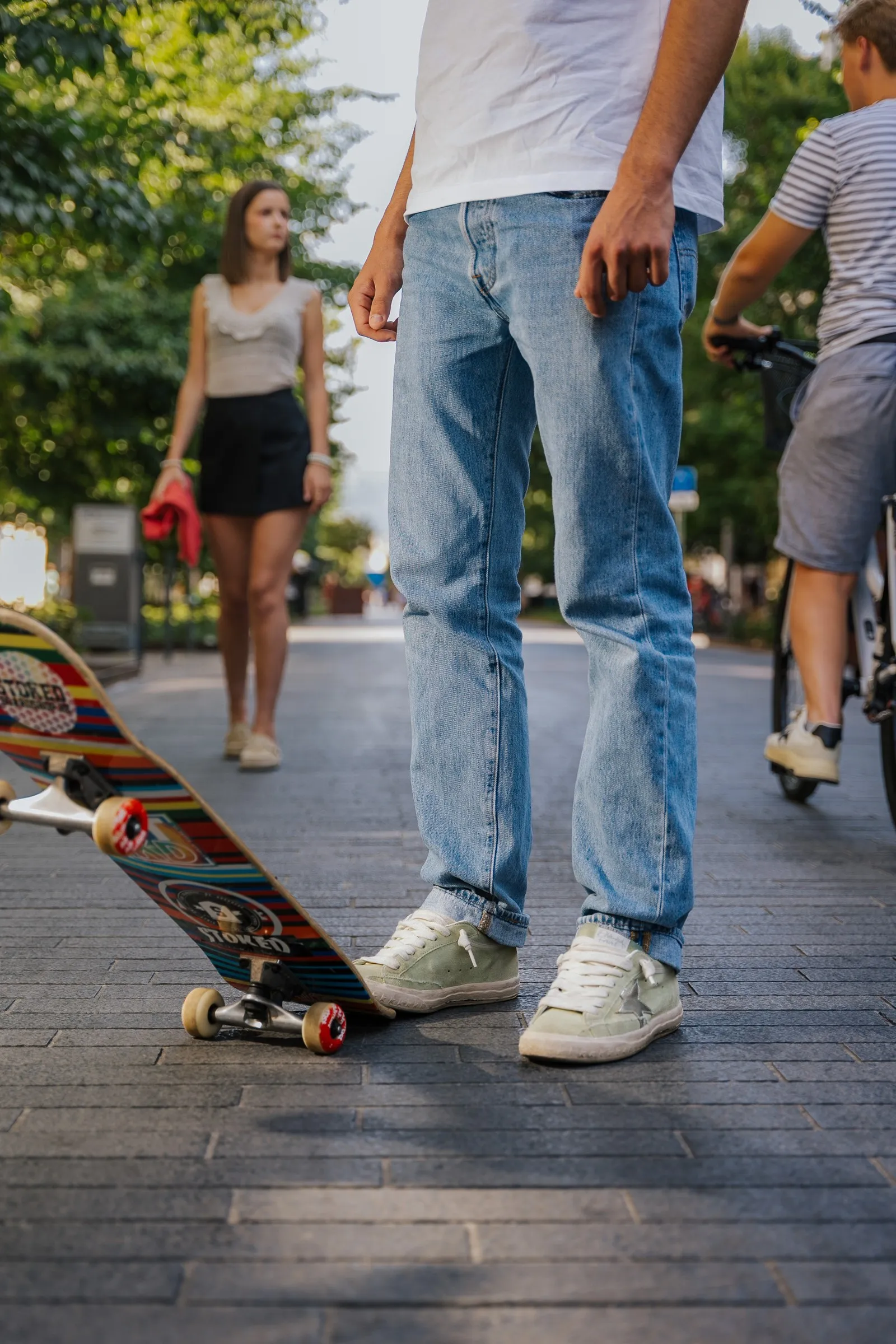 Skateboarder standing in a pedestrian street, framed at the legs