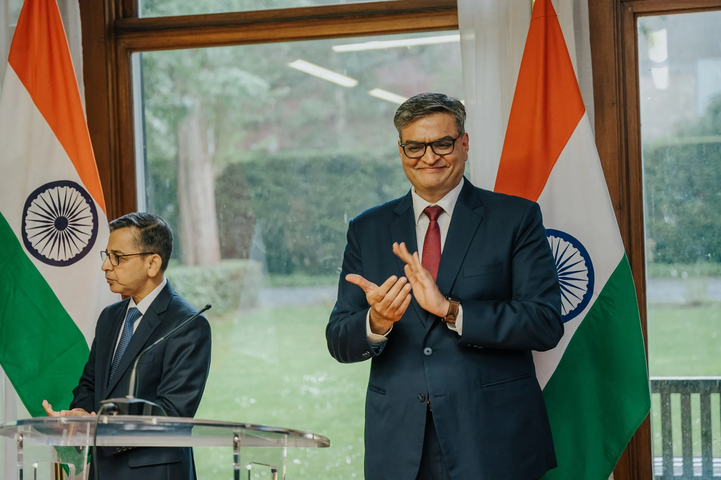 Speaker at the lectern and an official applauding in front of flags